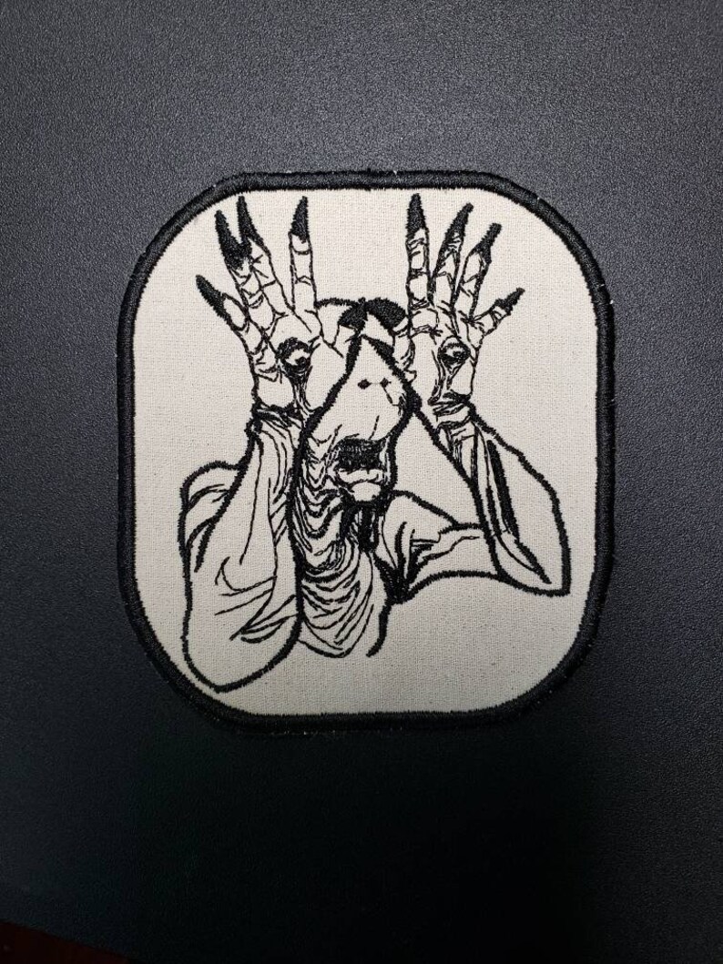 May include: Black and white embroidered patch of a creature with long fingers and a wide mouth, with a white background and black border.