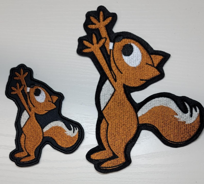 Peut inclure: Deux patchs brod&eacute;s thermocollants repr&eacute;sentant des &eacute;cureuils de dessin anim&eacute;. Le plus grand &eacute;cureuil est brun avec un ventre blanc et se tient debout sur ses pattes arri&egrave;re, les bras lev&eacute;s. Le plus petit &eacute;cureuil est brun avec un ventre blanc et se tient debout sur ses pattes arri&egrave;re, les bras le long du corps.