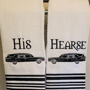 May include: Two white, textured hand towels with black embroidered text and images. One towel reads "His" above a black hearse illustration. The other reads "HEARSE" above a matching hearse. Both have black and white striped borders.