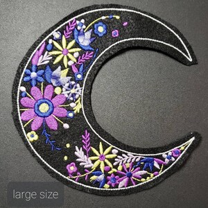 May include: A black felt crescent moon patch with embroidered purple, blue, and yellow flowers. The patch is outlined in white thread and has a "large size" label.