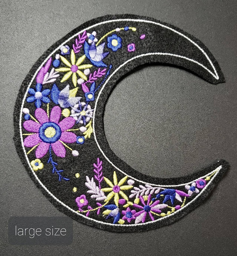 May include: A black felt crescent moon patch with embroidered purple, blue, and yellow flowers. The patch is outlined in white thread and has a "large size" label.