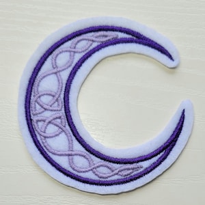 May include: A crescent moon patch with a white background and a purple border. The interior features a light purple Celtic knot design. The patch is likely made of fabric and is designed to be sewn or ironed onto clothing or accessories.