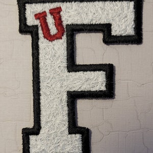 May include: White felt letter F with a black outline. The letter F has a red felt U in the top left corner.
