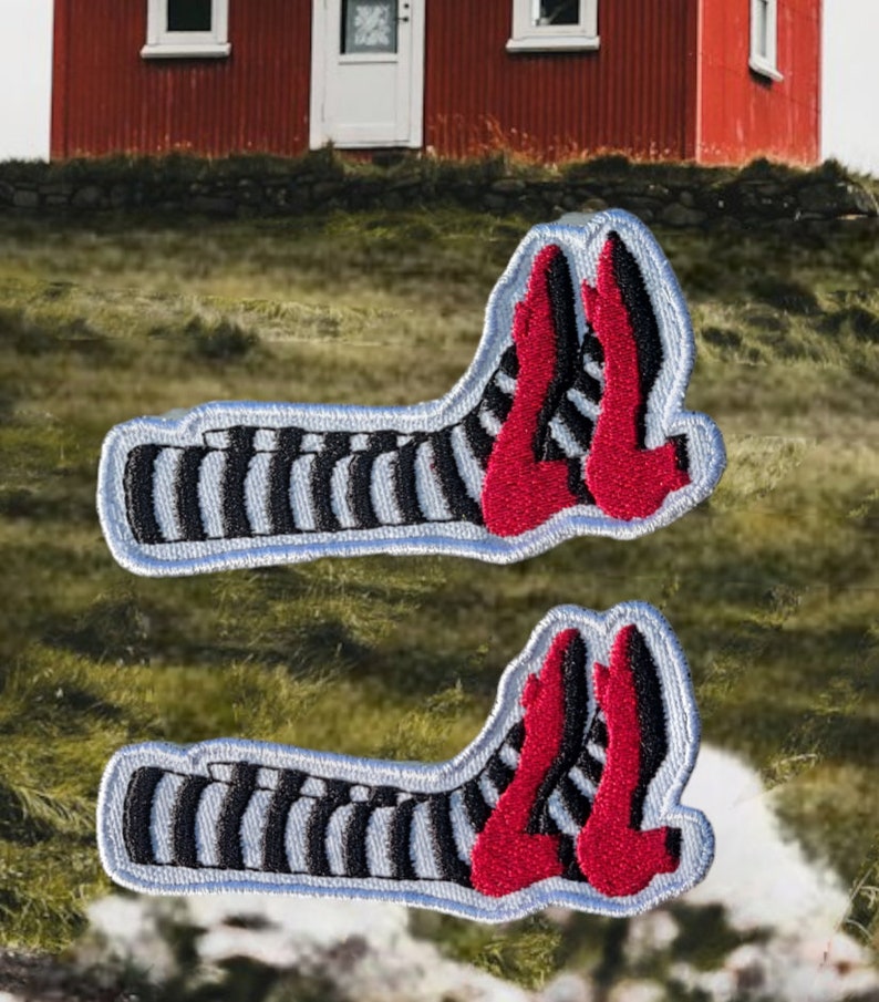 May include: Two embroidered patches featuring a pair of red high-heeled shoes and black and white striped legs. The patches have a light blue border and are set against a blurred outdoor background.
