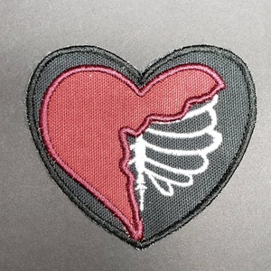 May include: A black heart-shaped patch with a red heart sewn on top. The red heart is partially torn, revealing a white skeletal wing underneath.