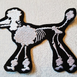 May include: White embroidered skeleton poodle patch on a black background.