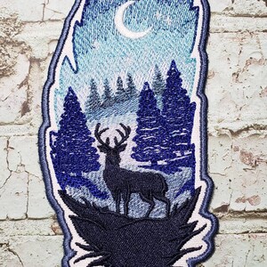 May include: Embroidered patch featuring a blue and white feather with a crescent moon, stars, and a silhouette of a deer in a forest scene.