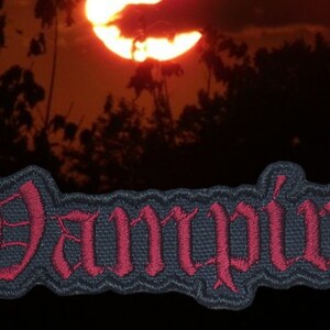 May include: A black and red embroidered patch with the word "Vampire" in a gothic font.