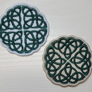 May include: Two green and white embroidered Celtic knot designs. The knots are circular and have a white background with green embroidery.