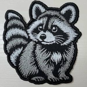 May include: A white ceramic mug with a black handle and the text "But First, Coffee" in a bold, black font. The mug is set against a blurred background, suggesting a cozy setting.