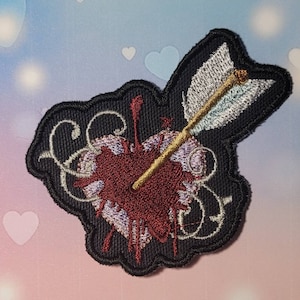 May include: Embroidered patch of a heart pierced by an arrow, with blood dripping from the wound. The heart is purple and red, the arrow is gold, and the background is black.