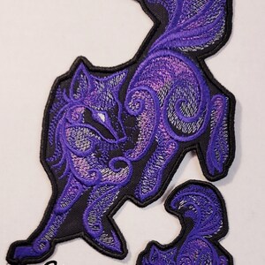 May include: Purple embroidered iron-on patch of a stylized wolf with a curled tail. The wolf is outlined in black and has a swirling pattern.