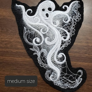 May include: White embroidered ghost with a black background. The ghost is in a swirling, lacy design. The text "medium size" is visible in the lower left corner of the image.