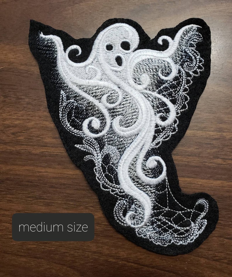 May include: White embroidered ghost with a black background. The ghost is in a swirling, lacy design. The text "medium size" is visible in the lower left corner of the image.