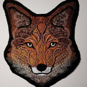 Peut inclure: Patch brod&eacute; repr&eacute;sentant la t&ecirc;te d'un renard avec des d&eacute;tails complexes dans des tons de brun, orange et blanc. Les yeux du renard sont verts et le fond est noir.