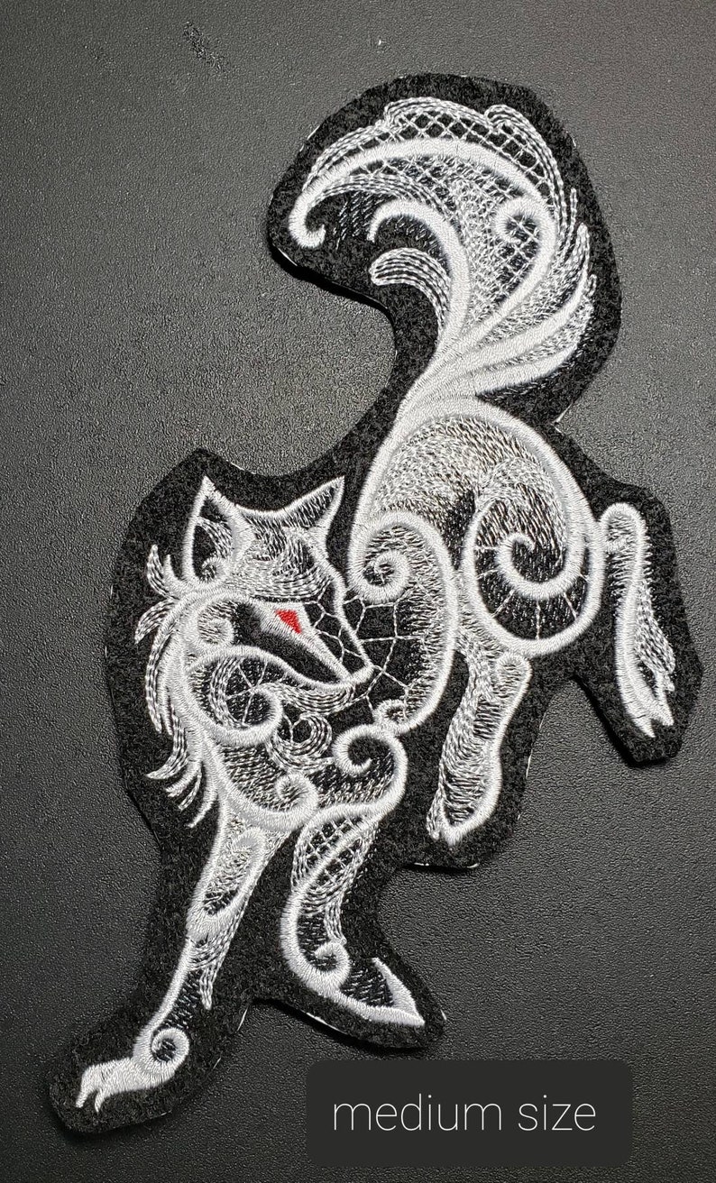 May include: White embroidered patch of a wolf with a red eye, with intricate details and a black background. The wolf is in a curled position with its tail curled around its body. The patch is medium size.
