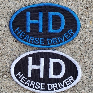 May include: Two black oval patches with white and blue embroidery. The patches read "HD HEARSE DRIVER".