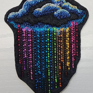 May include: Embroidered patch of a dark blue cloud with a rainbow of colorful raindrops falling from it. The patch is on a black felt background.