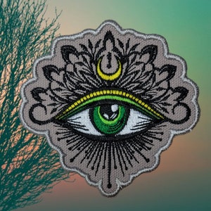 May include: Embroidered patch with a green eye, yellow and green eyelids, and a crescent moon above the eye. The eye is surrounded by a black and white floral design.