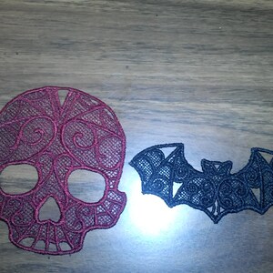 May include: A burgundy skull and a black bat, both made of lace, are displayed on a wooden surface. The skull has intricate floral patterns, while the bat has a detailed wing design. These decorative items are suitable for Halloween or gothic-themed crafts.