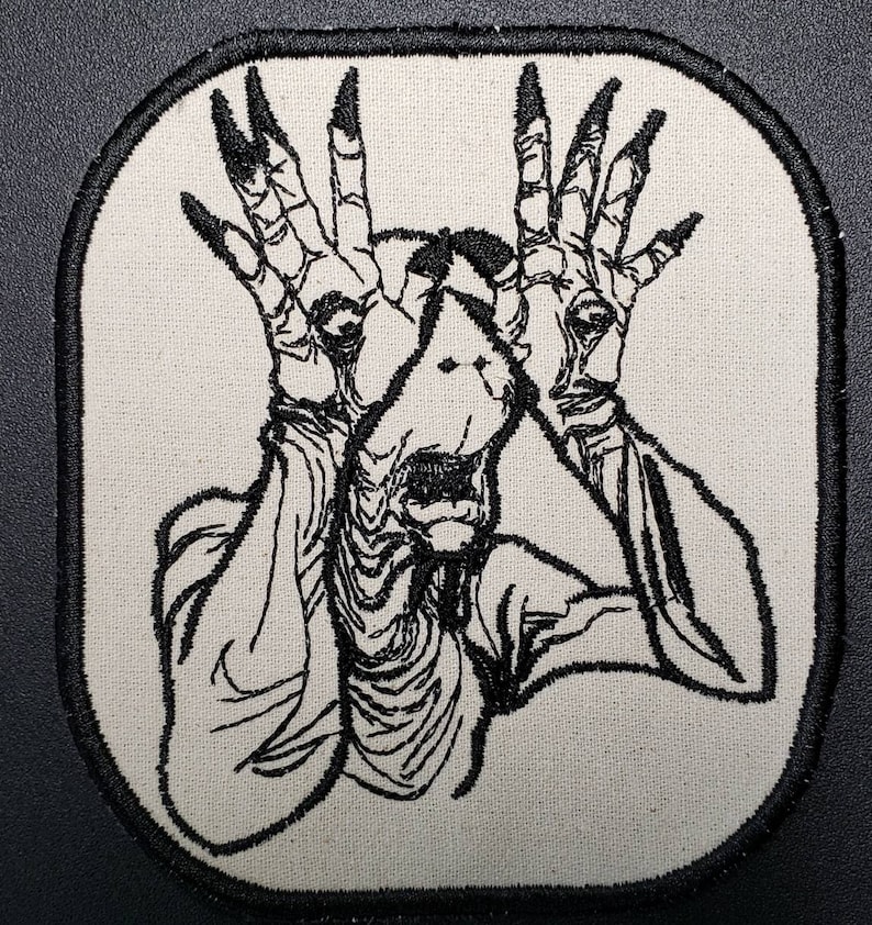 May include: Black and white embroidered patch of a creature with long fingers and a screaming face.