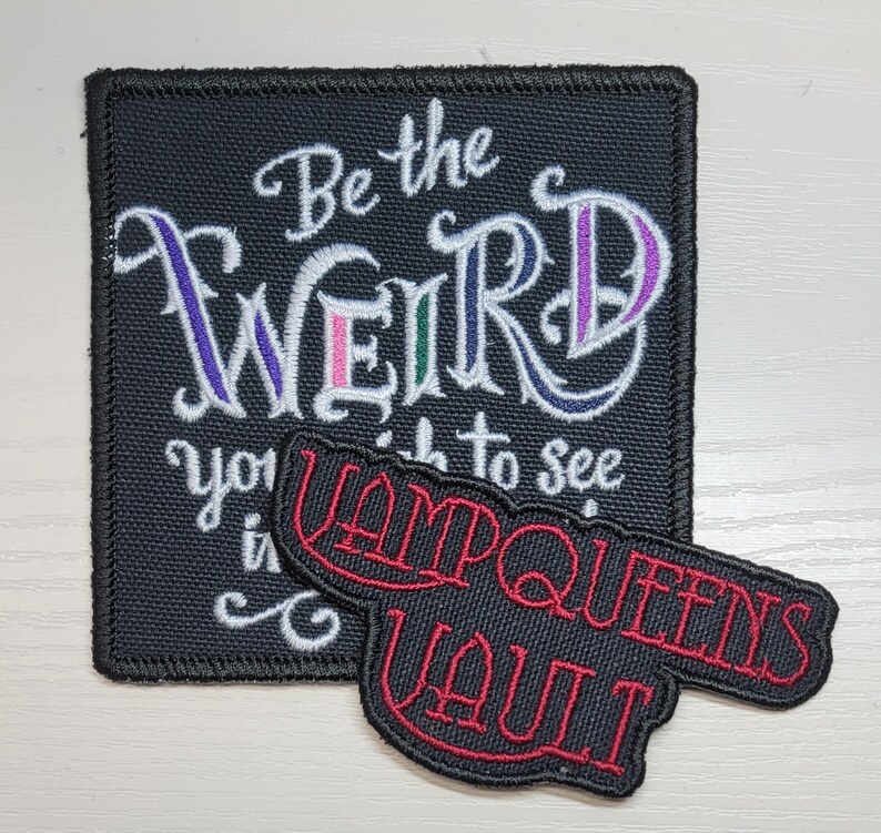Op de afbeelding: Zwarte en witte geborduurde patch met de tekst "Be the weird you wish to see in the world" en een rode geborduurde patch met de tekst "VampQueens Vault".