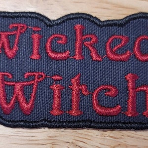May include: A black fabric patch with red embroidered text that reads "Wicked Witch".