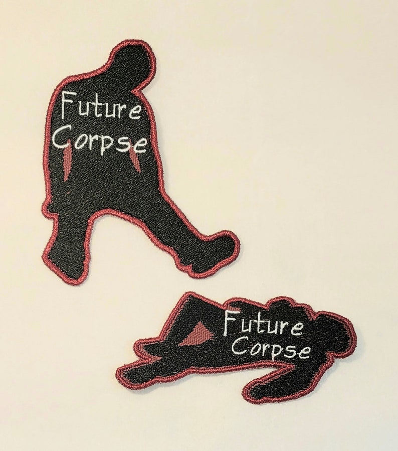 May include: Two black embroidered patches with red outlines. The patches are shaped like silhouettes of people. One patch shows a person walking and the other shows a person lying down. Both patches have the text "Future Corpse" in white.