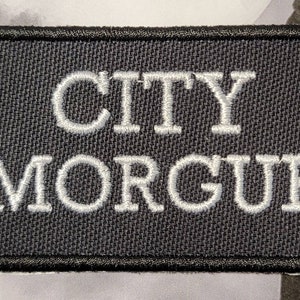 May include: Black embroidered patch with white stitching that reads "CITY MORGUE".