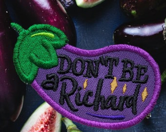Pode incluir: Etiqueta bordada em forma de berinjela roxa com o texto "Don't be a Richard" em letras pretas com detalhes amarelos. A etiqueta é cercada por berinjelas roxas e figos verdes.