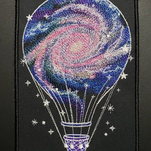 May include: Embroidered patch of a hot air balloon with a galaxy design. The balloon is filled with a swirling blue, pink, and white galaxy pattern. The balloon is surrounded by white stars on a black background.