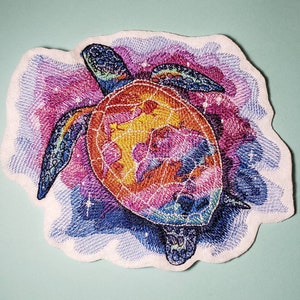 May include: A colorful embroidered patch of a sea turtle with a galaxy design. The turtle is a vibrant mix of pink, orange, yellow, and blue.
