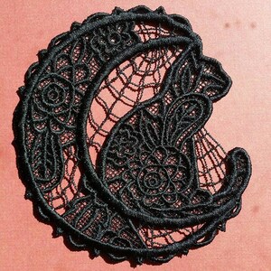 May include: Black lace applique in the shape of a crescent moon with a floral design. The lace is delicate and intricate, with a fine, thread-like texture.
