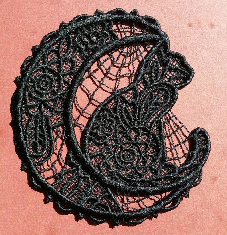 May include: Black lace applique in the shape of a crescent moon with a floral design. The lace is delicate and intricate, with a fine, thread-like texture.