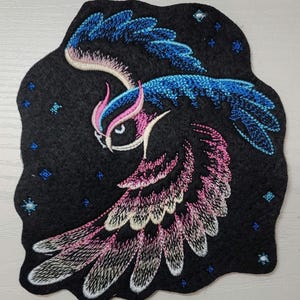 May include: Embroidered patch of a pink and blue owl flying against a black background with white stars.