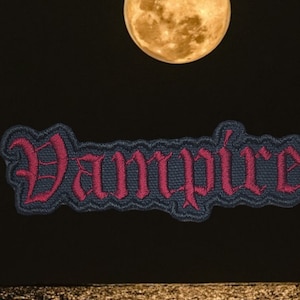 May include: A dark blue embroidered patch with the word "Vampire" in red lettering. The patch is against a black background with a full moon in the upper center of the image.