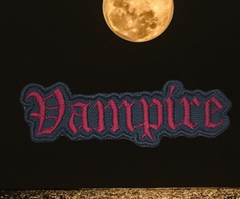 May include: A dark blue embroidered patch with the word "Vampire" in red lettering. The patch is against a black background with a full moon in the upper center of the image.