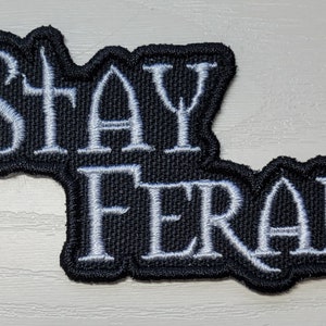 May include: Black embroidered patch with white stitching that reads "Stay Feral".
