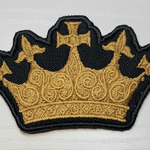 May include: A gold embroidered crown patch with a black background. The crown has a detailed design with intricate swirls and a cross at the top.
