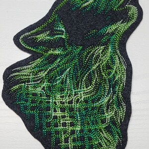 May include: Green embroidered wolf head patch on a dark gray felt background. The wolf is howling with its mouth open and its eyes closed.