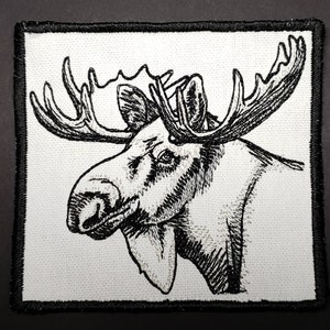 May include: Black and white embroidered patch of a moose head with large antlers. The moose is facing left and has a detailed, realistic design.