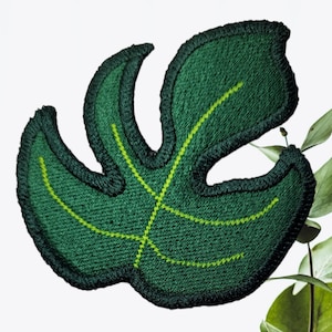 May include: Green felt embroidered patch of a monstera leaf with yellow stitching.