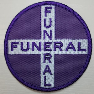 May include: A circular purple patch with the word "FUNERAL" in white, arranged in a cross shape. The patch has a stitched border and is likely an embroidered emblem.