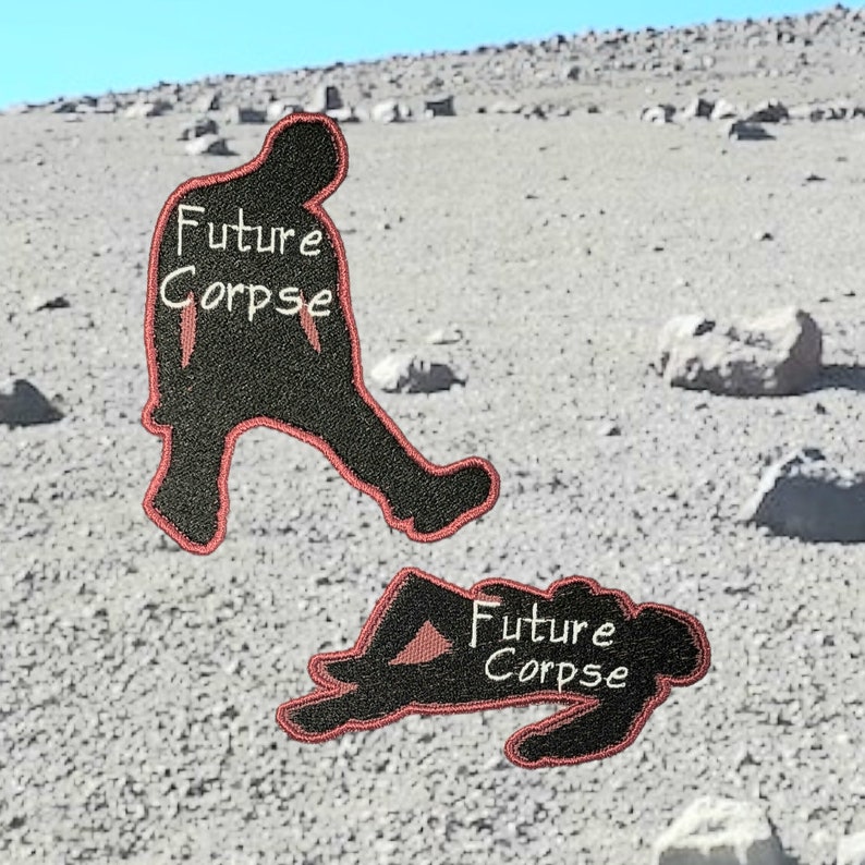 May include: Two black embroidered patches with red stitching. The patches are shaped like a person. One patch shows a person walking with the text "Future Corpse" written on the chest. The other patch shows a person lying down with the text "Future Corpse" written on the chest.