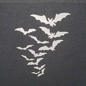 May include: A black fabric background with a cluster of white bats in a cascading pattern. The bats are cut out of paper or vinyl and are arranged in a way that suggests they are flying.