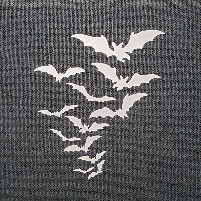 May include: A black fabric background with a cluster of white bats in a cascading pattern. The bats are cut out of paper or vinyl and are arranged in a way that suggests they are flying.
