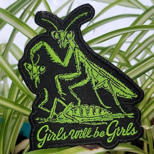 May include: Embroidered patch featuring a green praying mantis illustration on a black background. The mantis is depicted with intricate details. The phrase "Girls will be Girls" is embroidered in green script below the insect.