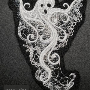 May include: White lace ghost applique with a small size label. The ghost is in a classic spooky pose with its arms outstretched and a face with two eyes and a mouth.