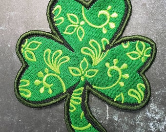 May include: A green shamrock patch with a detailed floral design. The shamrock is outlined in black and has a green stem.