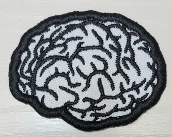 May include: Embroidered patch in the shape of a brain. The patch features a white background with black embroidered lines depicting the brain's structure. The patch is outlined with a thick black border.